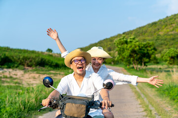 Happy Asian family couple riding motorcycle together while travel on tropical island mountain road in summer sunny day. Husband and wife enjoy outdoor lifestyle on holiday travel beach vacation