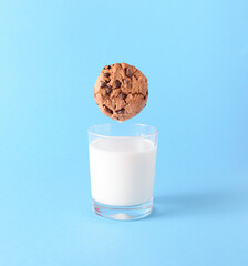 The chocolate chip cookie biscuit levitates in the air over a glass of milk on a blue background....