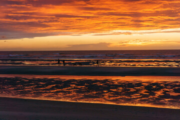 Beautiful sunset with dramatic moody cloudy sky above the ocean of North Sea and silhouette of people and dogs, De Haan, Belgium.