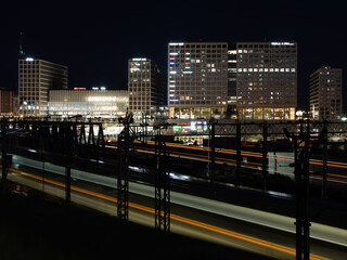 Modern financial district and a train station in the background. Passing by trains cast light trails in the foreground.
