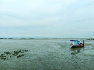Obraz premium A fishing boat stranded on the shore, the sky is white with clouds.