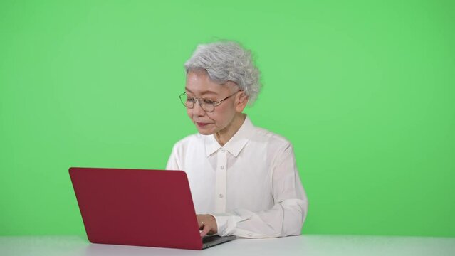 ノートパソコンを使うシニア女性　クロマキー合成用グリーンバック