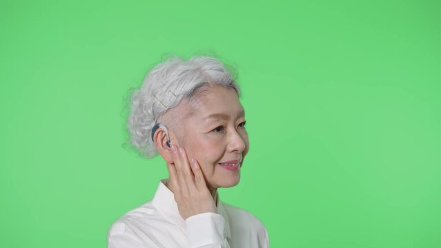 補聴器をつけるシニア女性　クロマキー合成用グリーンバック