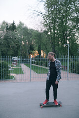 Casual man with longboard on sunset. Hipster skater holding skateboard. Young guy with mustache and beard longborading in park