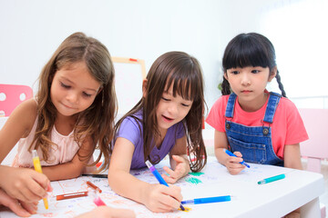 Happy caucasian and Asian young elementary school age enjoy learning and playing in their classroom with their teacher. Boys and girls studying arts and mathematics in classroom.