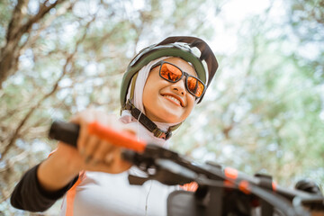 Naklejka premium bottom view of attractive veiled girl in sunglasses smiling while riding bicycle in park