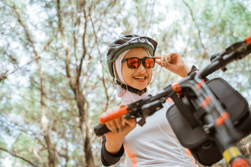 veiled asian girl holding sunglasses smiling while cycling in park