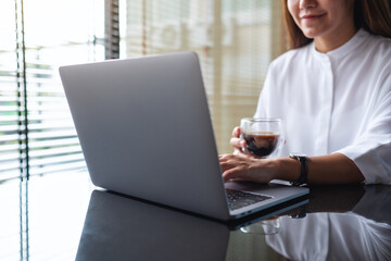 Closeup image of a business woman working on laptop computer while drinking coffee in office