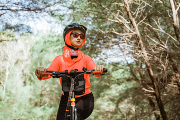woman in red jacket cycling in park with trees in the background