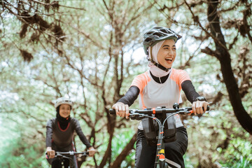 Happiness of beautiful young muslim woman wearing sportswear and helmet while cycling together outdoors