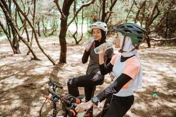 Fototapeta na wymiar Two young Muslim women drinking mineral water bottles while cycling under a shady tree