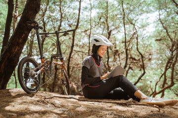 veiled girl sitting resting cycling wearing earphones and using tablet while in the park