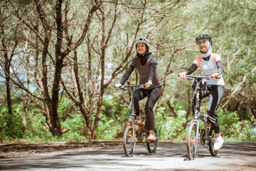 Two attractive Muslim women enjoying cycling together on the road with trees in the background