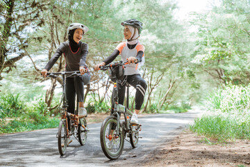 Naklejka premium Two Muslim women wearing sportswear and cycling helmets on the street on the outdoor background