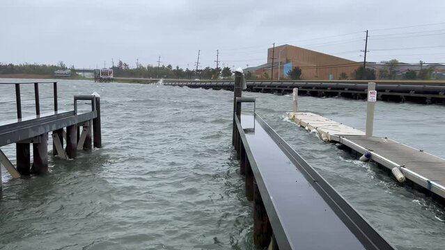 Rough bay water crashes against bulkhead as cars rush by during a storm