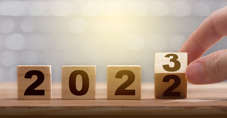 Fingers turning the block from 2022 to 2023. New year concept. Figures of the year 2023 on a wooden...
