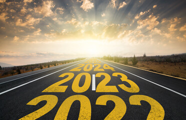 The word 2023 written on highway road in the middle of empty asphalt road at golden sunrise. New...