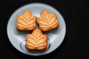 Delicious cookies filled with vanilla cream made with honey or maple syrup from Canadian trees, the traditional sweet of Canada in white plate on a black bakground
