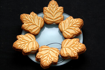 Delicious cookies filled with vanilla cream made with honey or maple syrup from Canadian trees, the traditional sweet of Canada in white plate on a black bakground
