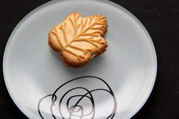 Delicious cookies filled with vanilla cream made with honey or maple syrup from Canadian trees, the traditional sweet of Canada in white plate on a black bakground
