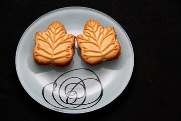 Delicious cookies filled with vanilla cream made with honey or maple syrup from Canadian trees, the traditional sweet of Canada in white plate on a black bakground
