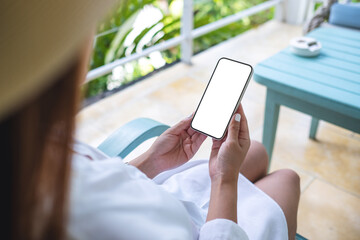 Mockup image of a woman holding mobile phone with blank white desktop screen while sitting and...