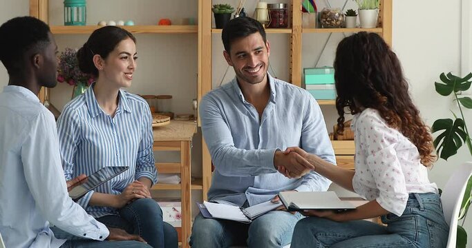 Young Latin woman hold paper planner propose effective solution innovative decision to department staff gathered on meeting. Male team leader shake female worker hand impressed with good idea offered