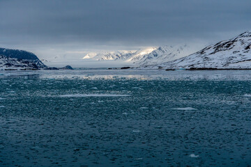 Sea with melting ice cubes, snowy mountains In Svalbard, Norway. Global Warming.