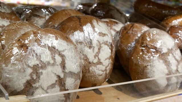 Close-up of many beautiful packaged rye loafs on a wooden counter and a male hand takes one