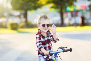 stylish European boy in a shirt and dark glasses rides a balance bike on the asphalt. Fashionable...