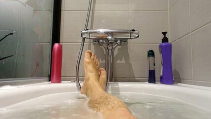 Feet sticking out of the water and soap suds during a hot bath in the tub.