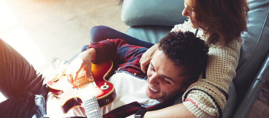 Obraz premium Happy couple domestic life situation. Wife and husband in love playing guitar sitting on couch together