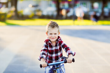 stylish European boy in shirt and jeans rides balance bike on asphalt. Child riding without helmet