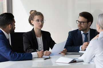 Serious young business professional woman speaking at corporate meeting, analyzing paper document, giving expertise, consultation. Female boss, team leader instructing group