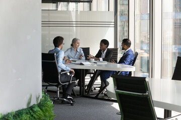 Multiethnic business team discussing project in meeting room. Female corporate leader instructing employees. Diverse group of partners negotiating on deal, startup in urban office. Wide shot