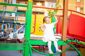 a happy child girl plays at the children's complex playground near the house in the summer in the yard and smiles