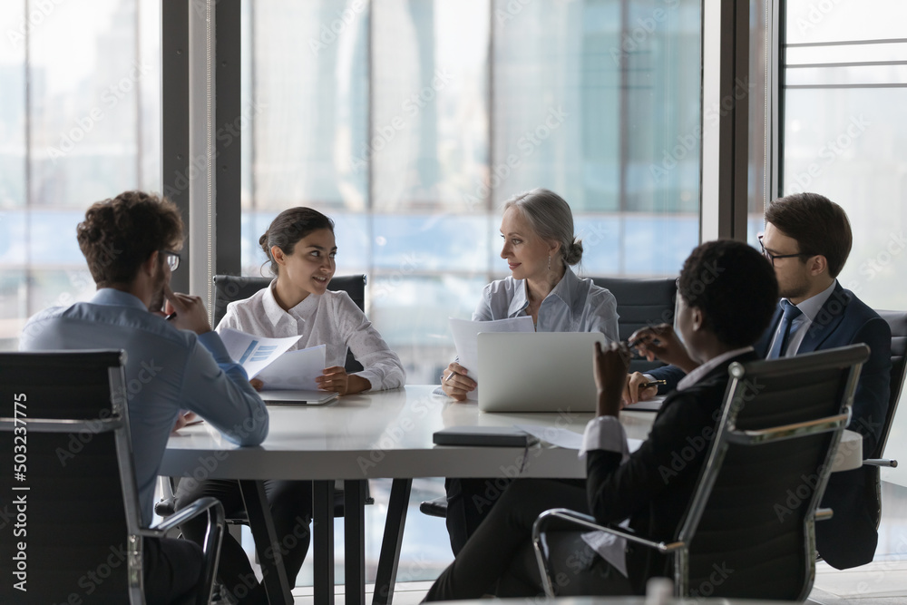 Wall mural Multiethnic business team working together, brainstorming, discussing project, talking at table in meeting room. Startup managers, investors analyzing marketing data, stats report