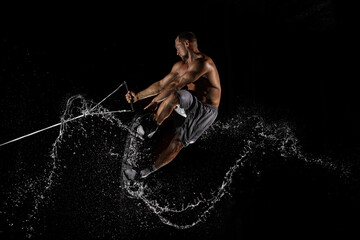 A man practices trampolining on a rubber board for kitesurfing on the water against a black...