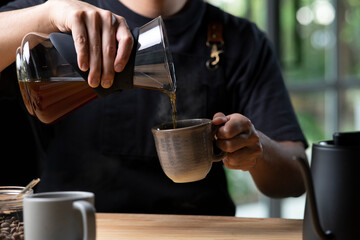 Barista pouring steaming drip coffee with smoke in to a cup on a work desk in coffee shop