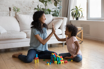 Joyful excited African mom and little kid celebrating playing achieve, giving high five over toy...