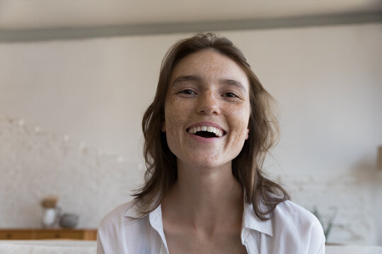 Excited cheerful freckled blogger girl head shot screen view portrait. Happy pretty young woman talking on video call, looking at camera with toothy smile, laughing, enjoying live stream, broadcasting