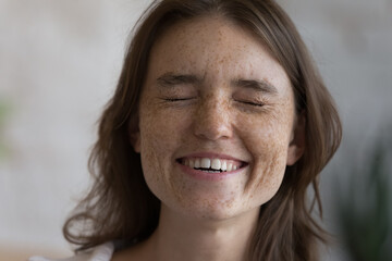 Cheerful excited freckled teen girl laughing with closed eyes. Happy overjoyed young woman with...