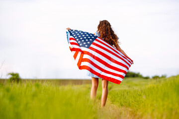 Young woman proudly hold waving american USA flag on blooming meadow.  4th of July. Fourth of July. Freedom. Patriotic holiday. Independence Day.