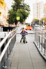 Stylish cute european boy on balance bike in the city, child rides a balance bike on ramp. Summer in the city, comfortable safety urban environment