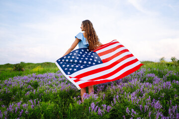 Young woman proudly hold waving american USA flag on blooming meadow.  4th of July. Fourth of July....