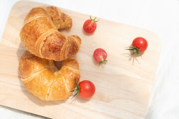 Croissant with red tomatoes isolated on wooden plate, fresh baked bread for easy breakfast.