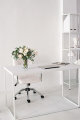 Office environment. A white room with a desk on which there is a vase, a laptop and magazines