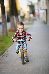 Stylish boy ride on balance bike on sidewalk in city