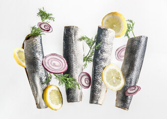 Flying raw fishes with flavoring ingredients: herring fillet, lemon, red onion and dill  at white...
