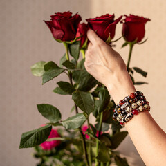 A woman's hand with bracelets made of jasper, obsidian and tiger's eye stones touches a bouquet of...